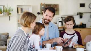 Eine Mutter und ein Vater sind mit ihren beiden Kindern am Frühstücken und diskutieren gemeinsam über das Taschengeld.